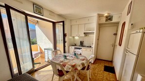 A compact kitchen with white cabinets, a dining table with chairs, and a refrigerator.