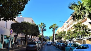 A street lined with parked cars, palm trees, and buildings with balconies.