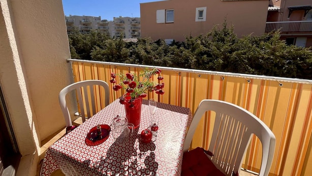 A balcony with a table and chairs, a potted plant, and a view of buildings in the background.