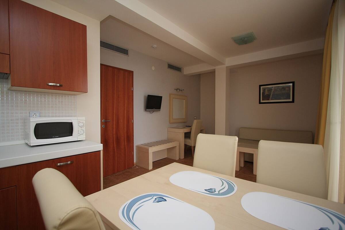 A hotel room with a kitchenette, a dining area with a table and chairs, a television, and a framed picture on the wall.