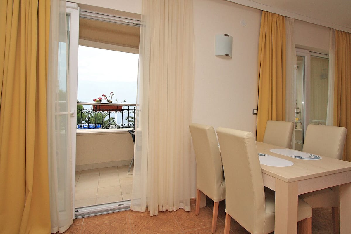 A hotel room with a balcony, a dining table with chairs, and a view of the sea.