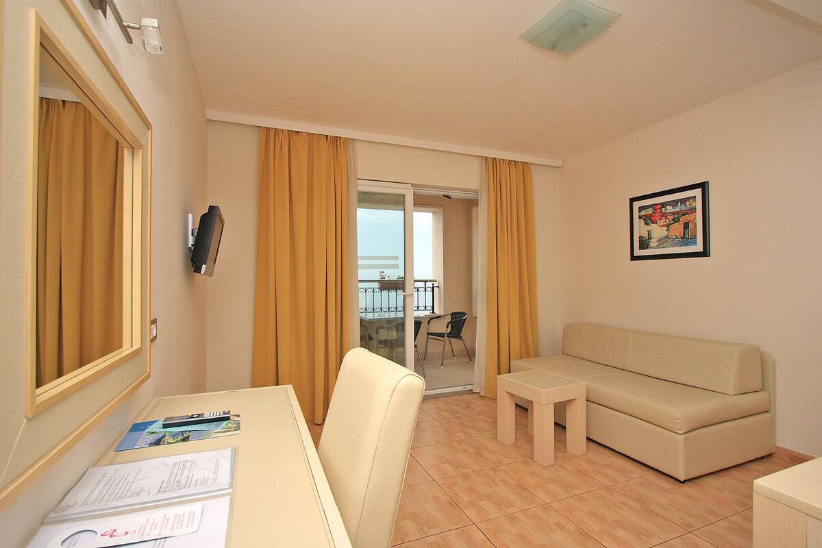 A hotel room with a sofa, a small table, a mirror, a phone, and a window with curtains.