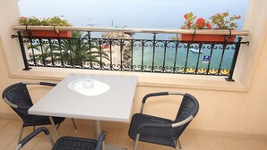 En balkon med bord og stole, der giver udsigt over kysten under en klar himmel.