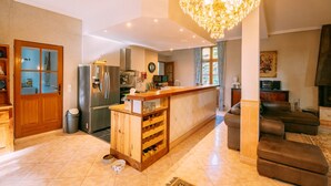 A spacious living area with a wooden bar, a chandelier, and a seating area with leather sofas. - Le Moulin du Pont (Mezin)