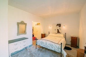 A bedroom with a bed, a dresser, a mirror, and a painting on the wall.