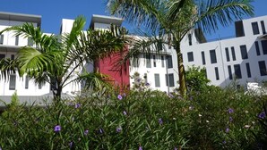 Un edificio moderno con fachadas blancas y rojas, rodeado de exuberante follaje y flores moradas.