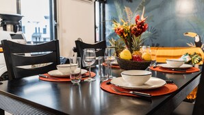 Una mesa de comedor preparada con platos, tazones, vasos y una cesta de frutas.