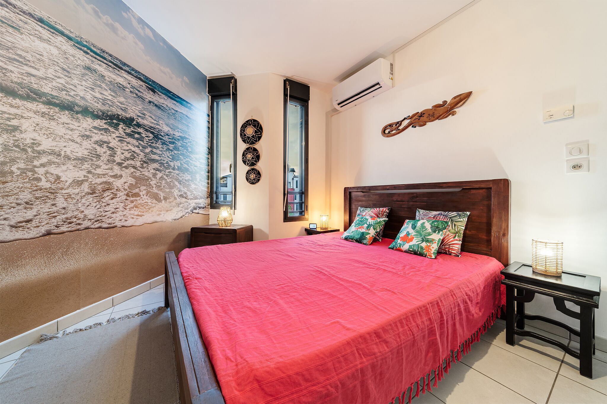 A bedroom with a large bed, a wooden headboard, a nightstand, a wall-mounted air conditioner, and a beach mural.