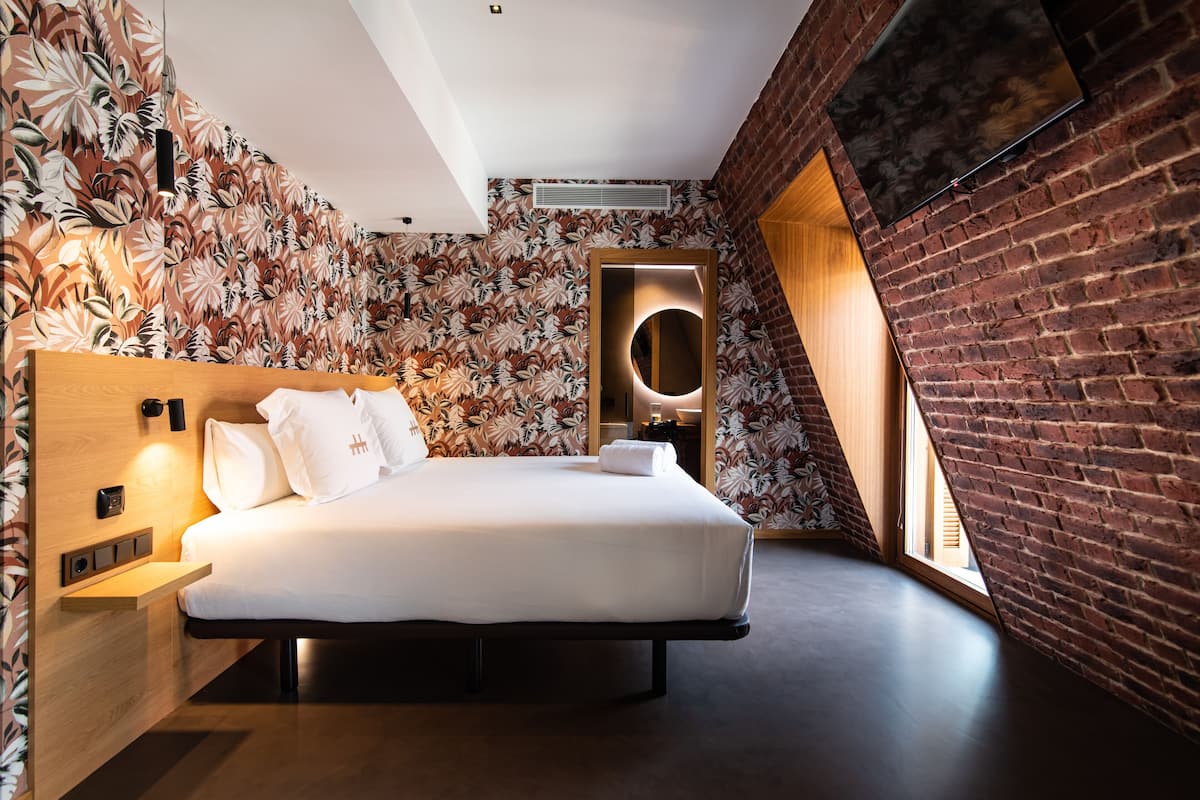 A modern bedroom with a large bed, a wooden headboard, a wall-mounted TV, and a brick wall.