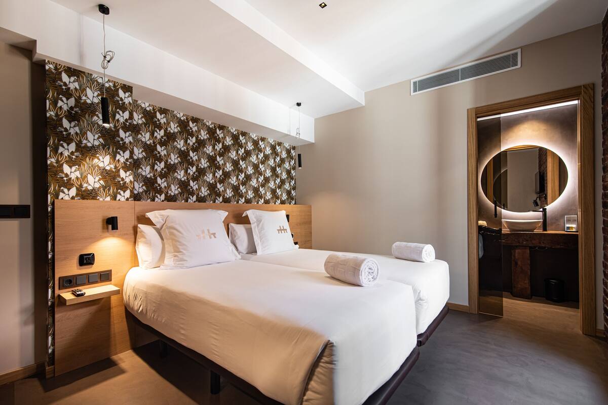 A modern hotel room with a large bed, a bedside table, a mirror, and a wall with a floral pattern.