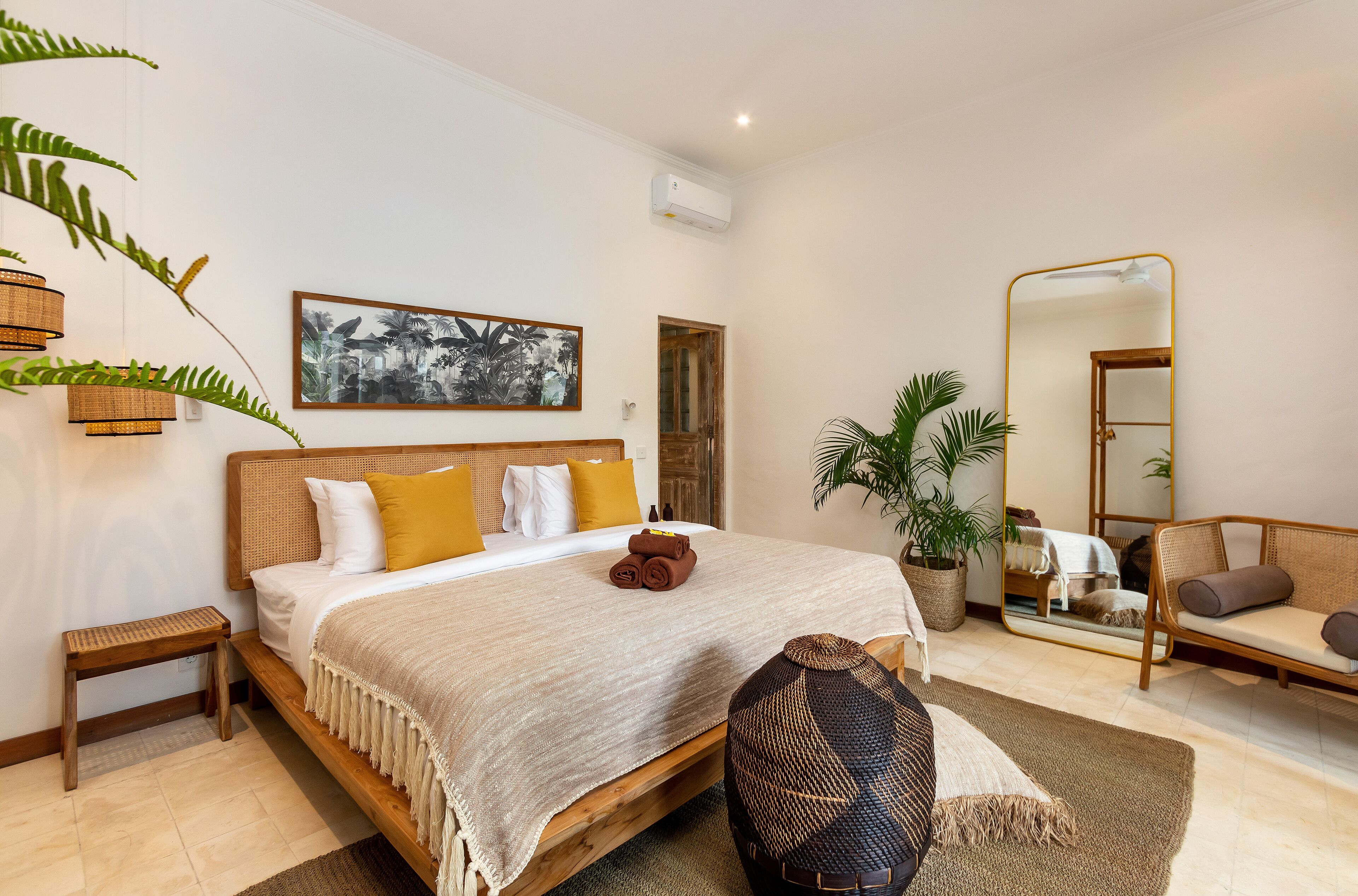 Un dormitorio con cama, mesitas de noche, un espejo, un sofá y una planta en maceta.