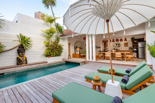 A poolside area with lounge chairs, a statue, and a dining area with a kitchen in the background.