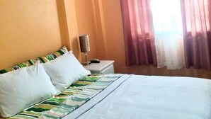 Une chambre à coucher comprenant un lit, une table de chevet, un climatiseur et une fenêtre avec des rideaux.