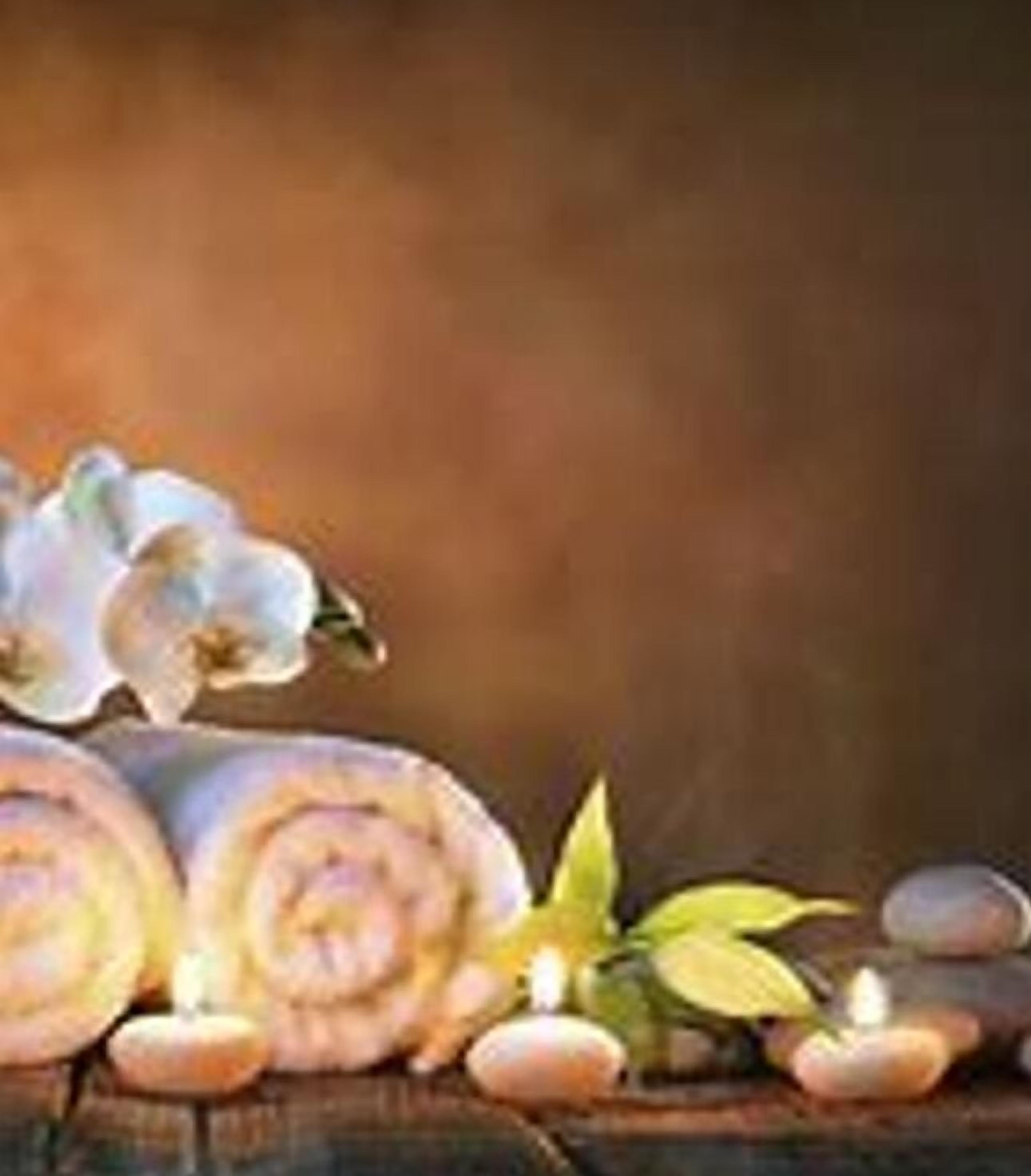 A wooden surface with rolled towels, a white orchid, and a small plant.