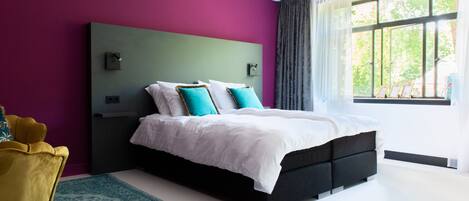 A modern bedroom with a black bed, white bedding, and teal pillows.