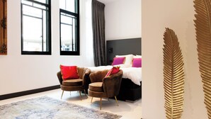 A hotel room with a bed, two armchairs, a large window, and a decorative leaf pattern on the wall. - De Salon van Fagel (The Hague)