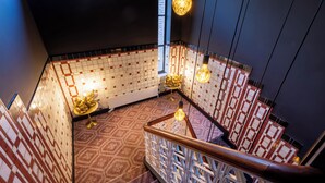 A staircase with patterned tiles, a decorative table, and hanging light fixtures. - De Salon van Fagel (The Hague)