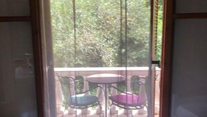 Ein Zimmer mit Bett, einem fenster mit Vorhängen und einem Balkon mit zwei Stühlen und einem Tisch.