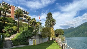 A waterfront property with a well-maintained lawn, a stone pathway leading to a building, and a view of the lake and mountains. - Lugano Blue Marine On Lake Shore (Lugano)