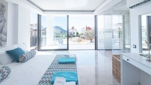 Un dormitorio moderno con una cama grande, un sofá y vistas al exterior a través de puertas de vidrio.