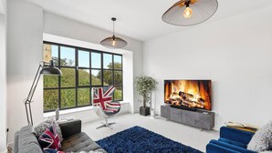 Una sala de estar moderna con un ventanal grande, una chimenea, un televisor y una bandera.
