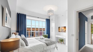 Un dormitorio moderno con un ventanal grande, una cama con un edredón blanco mullido, un escritorio y una silla verde.