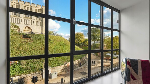 Un ventanal grande con vista a un edificio histórico y una colina cubierta de hierba.