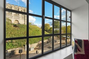 Un ventanal grande con vista a un edificio histórico y una colina cubierta de hierba.