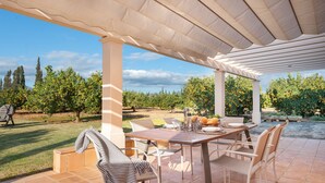 Een terras buiten met een eettafel, omringd door stoelen, en een pergola erboven.