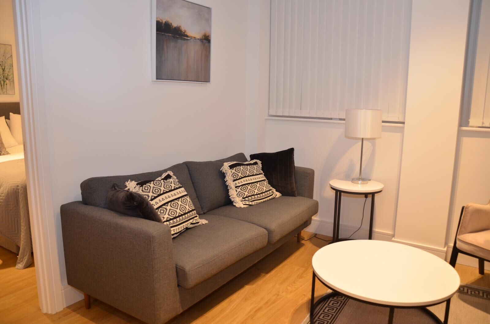 A modern living room with a grey sofa, patterned cushions, a small round table, and a lamp.