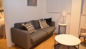 A modern living room with a grey sofa, patterned cushions, a small round table, and a lamp. - LARPOTE LODGE - LUTON (LUTON)