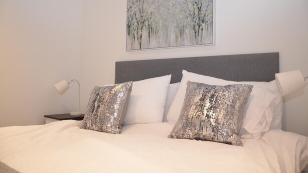 A neatly made bed with white linens and two decorative pillows, a bedside lamp, and a painting on the wall. - LARPOTE LODGE - LUTON (LUTON)