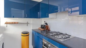 A kitchen with blue cabinets, a gas stove, and a yellow trash bin.