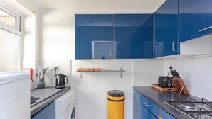 A compact kitchen with blue cabinets, a yellow trash bin, a coffee maker, and a toaster.