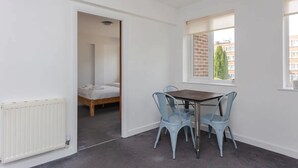 A room with a bed, a table with chairs, a window with a view of buildings, and a radiator.