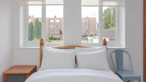 A bedroom with a bed, two windows, a chair, and a small table.