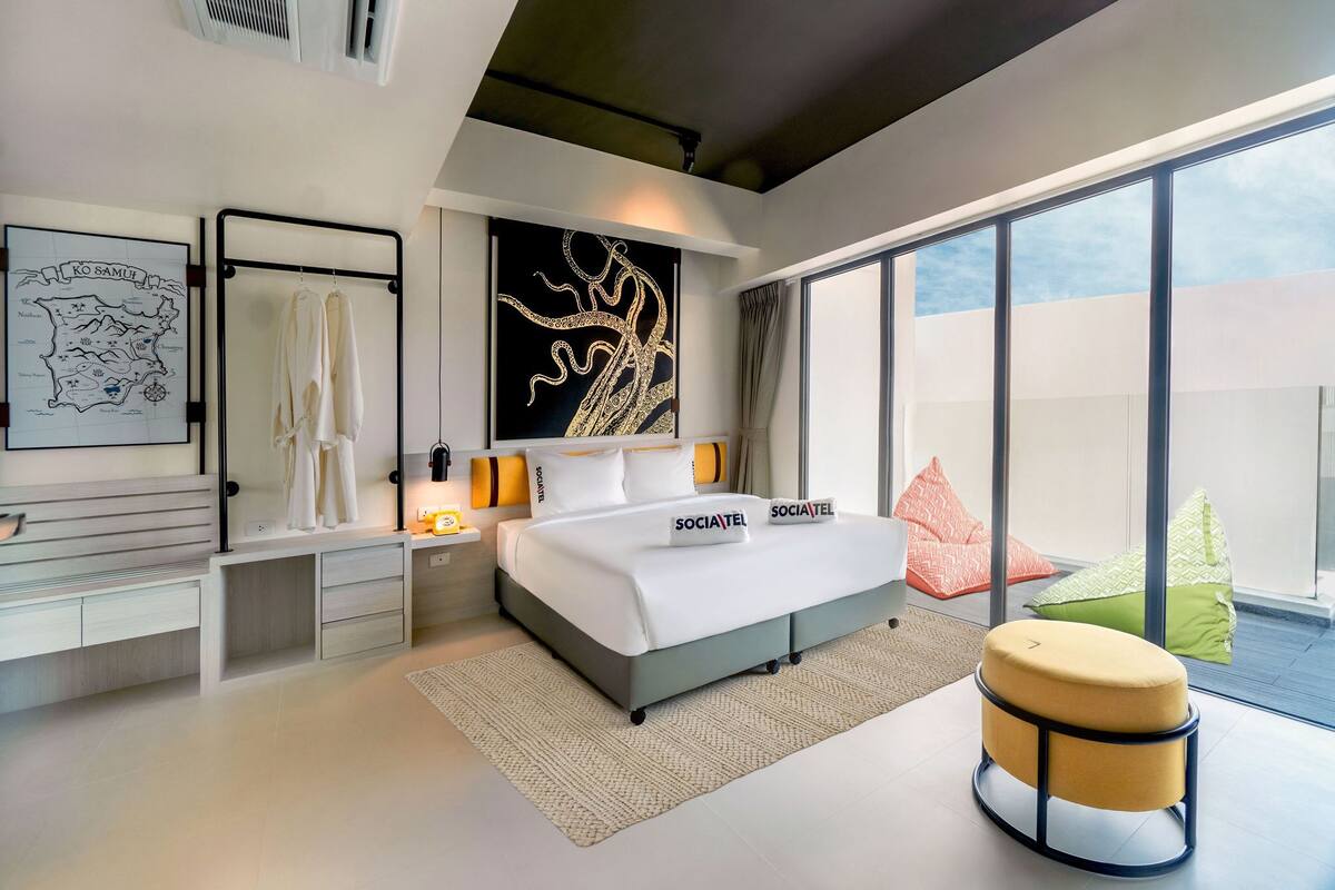 Une chambre à coucher moderne, dotée d’un grand lit, d’un bureau et offrant une vue sur le ciel grâce à de grandes fenêtres.