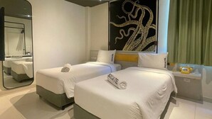 Una habitación de hotel moderna con dos camas, un espejo grande, un adorno en la pared y una mesita de noche con teléfono.