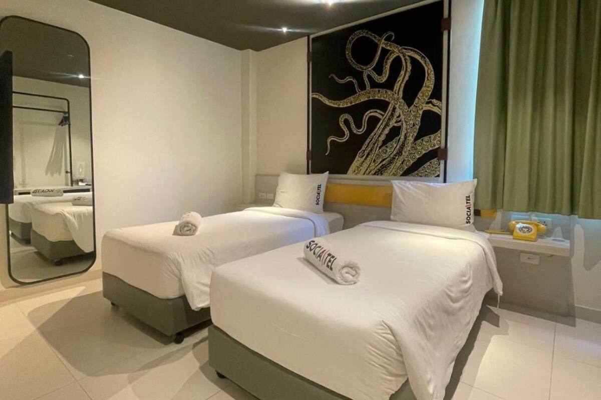Une chambre d’hôtel moderne avec deux lits, un grand miroir, un élément décoratif mural et une petite table de chevet avec un téléphone.