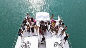 Un bateau avec un pont blanc et des motifs noirs décoratifs, rempli de personnes profitant d’une journée ensoleillée sur l’eau.