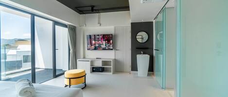 A modern hotel room with a large bed, a seating area with a small table, a television, and a bathroom with a sink and mirror.
