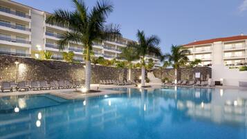 A hotel pool area with lounge chairs, palm trees, and a stone wall.