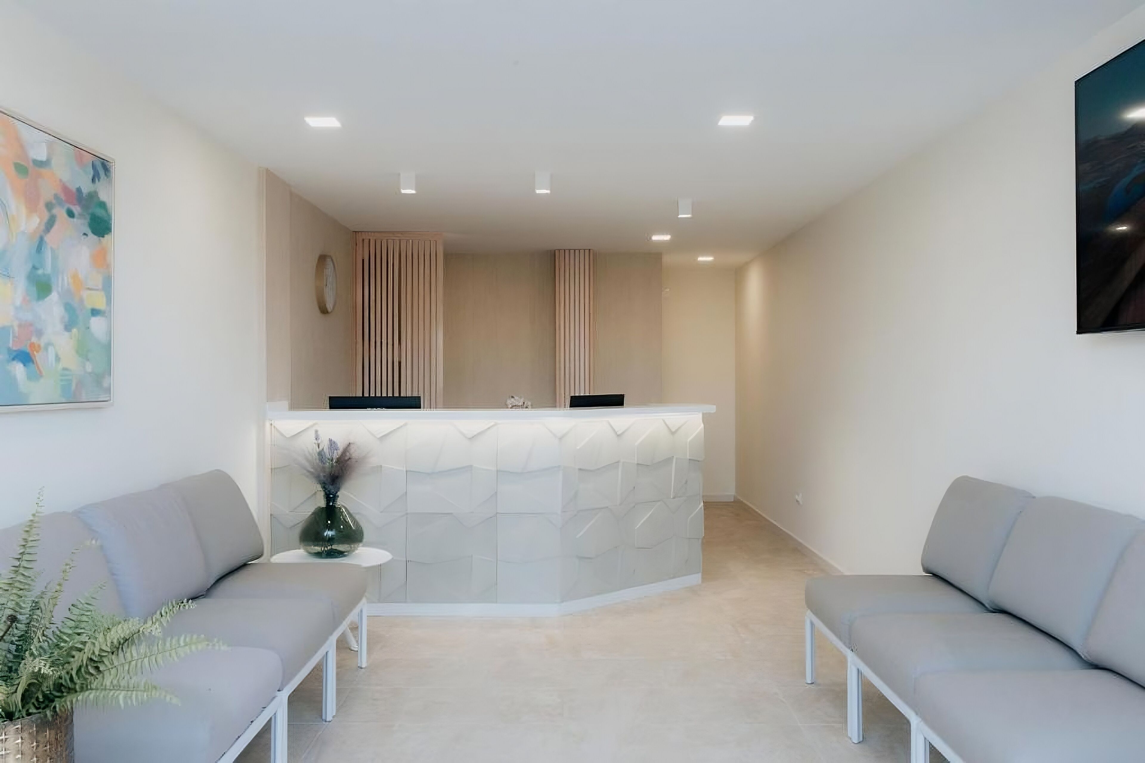 A reception area with a modern design, featuring a reception desk, two sofas, a small table with a vase, and a painting on the wall.