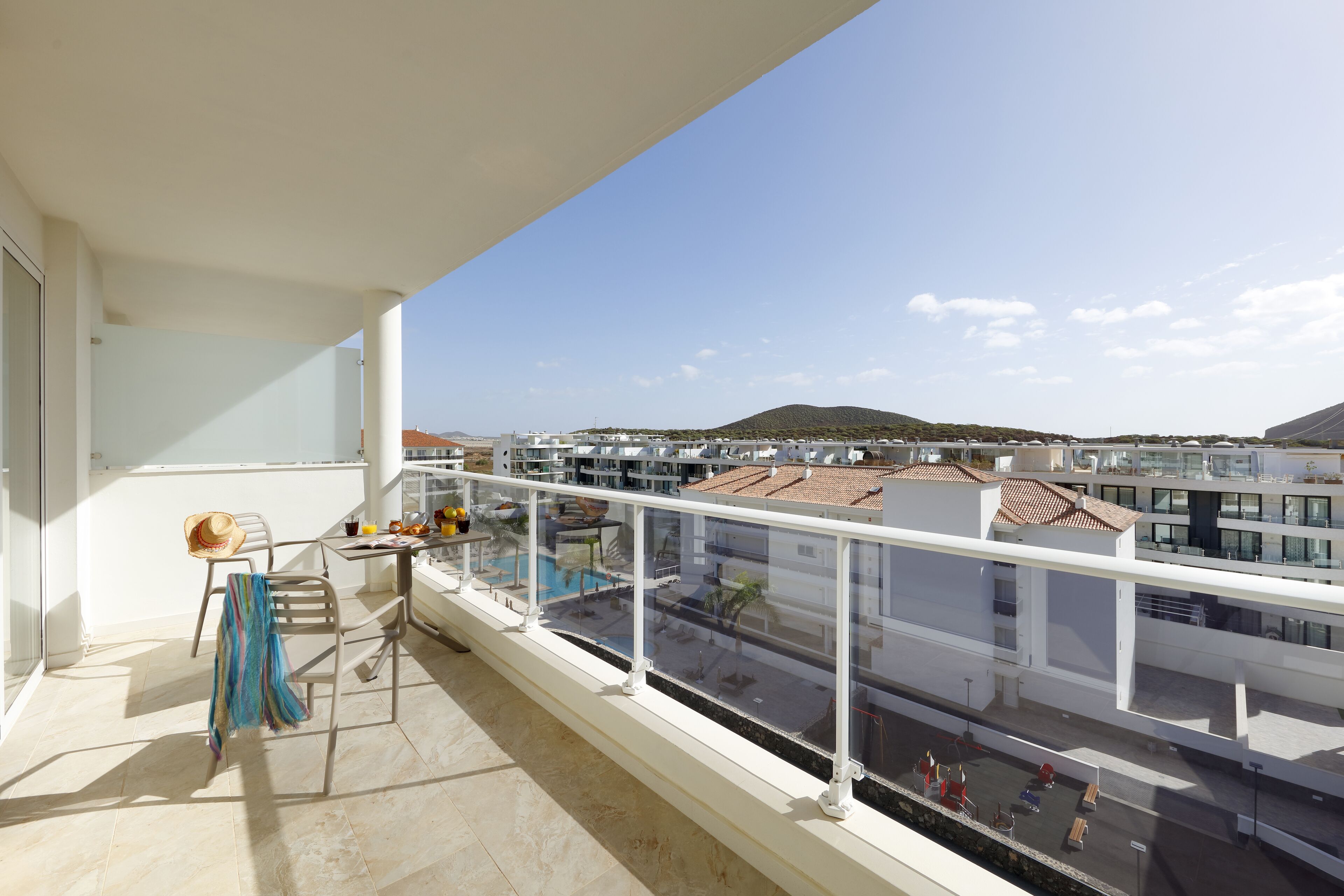 Ein Balkon mit Blick auf eine Wohngegend, ein Tisch mit Hut und einem gestreiften Tuch, und ein Stuhl.