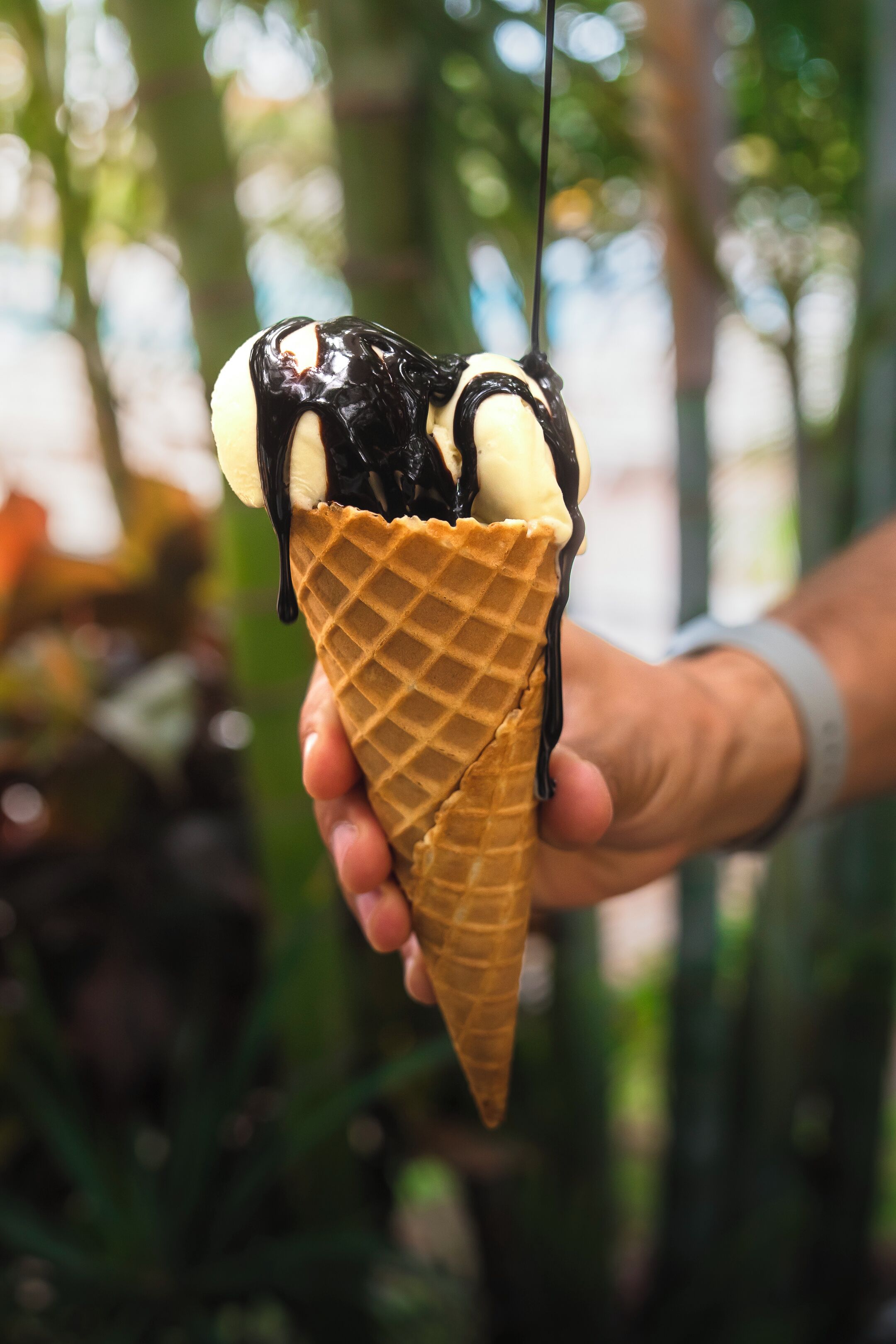 A hand holding a waffle cone with chocolate and banana toppings.