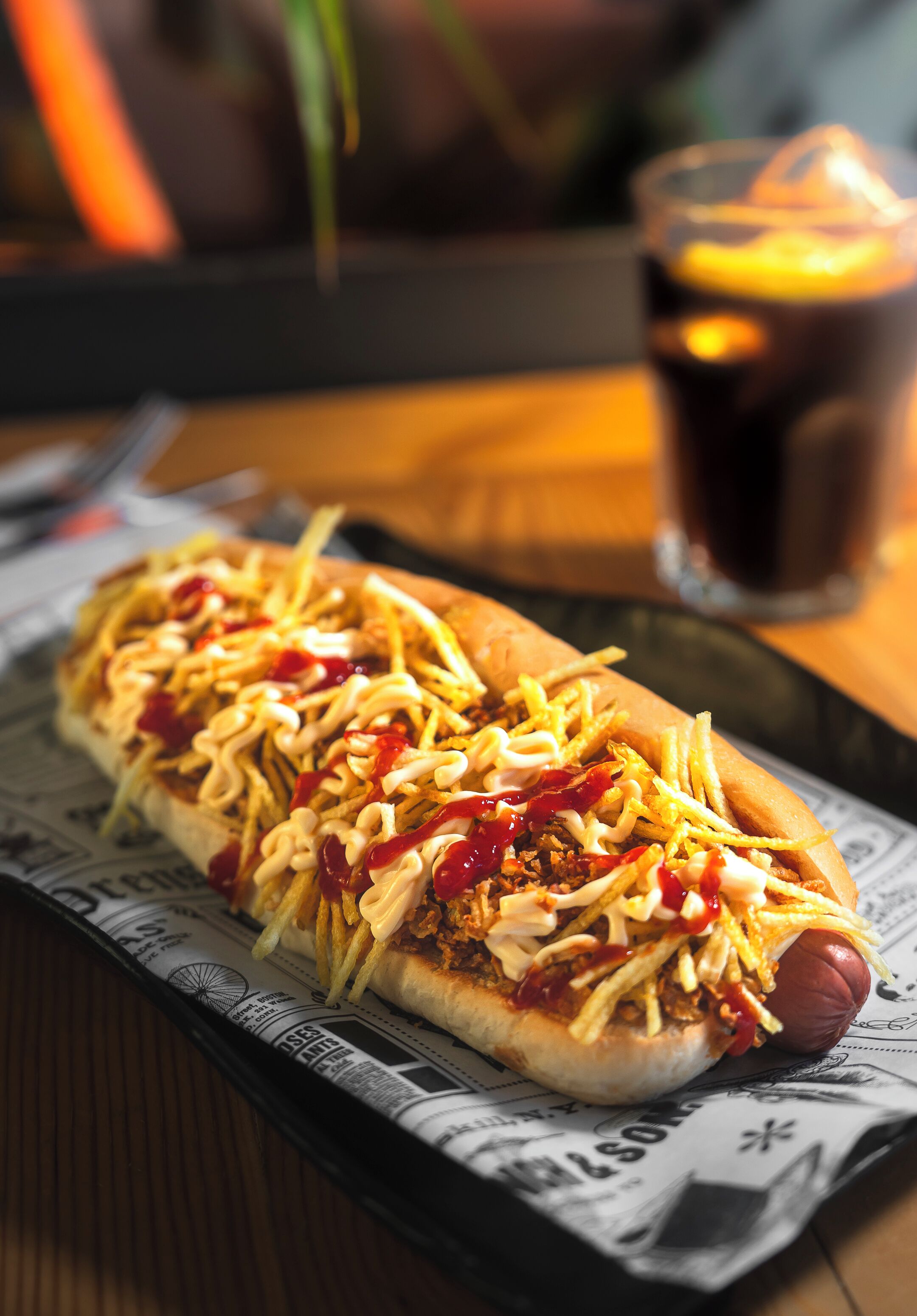 A hot dog with toppings on a bun, placed on a newspaper-lined tray.