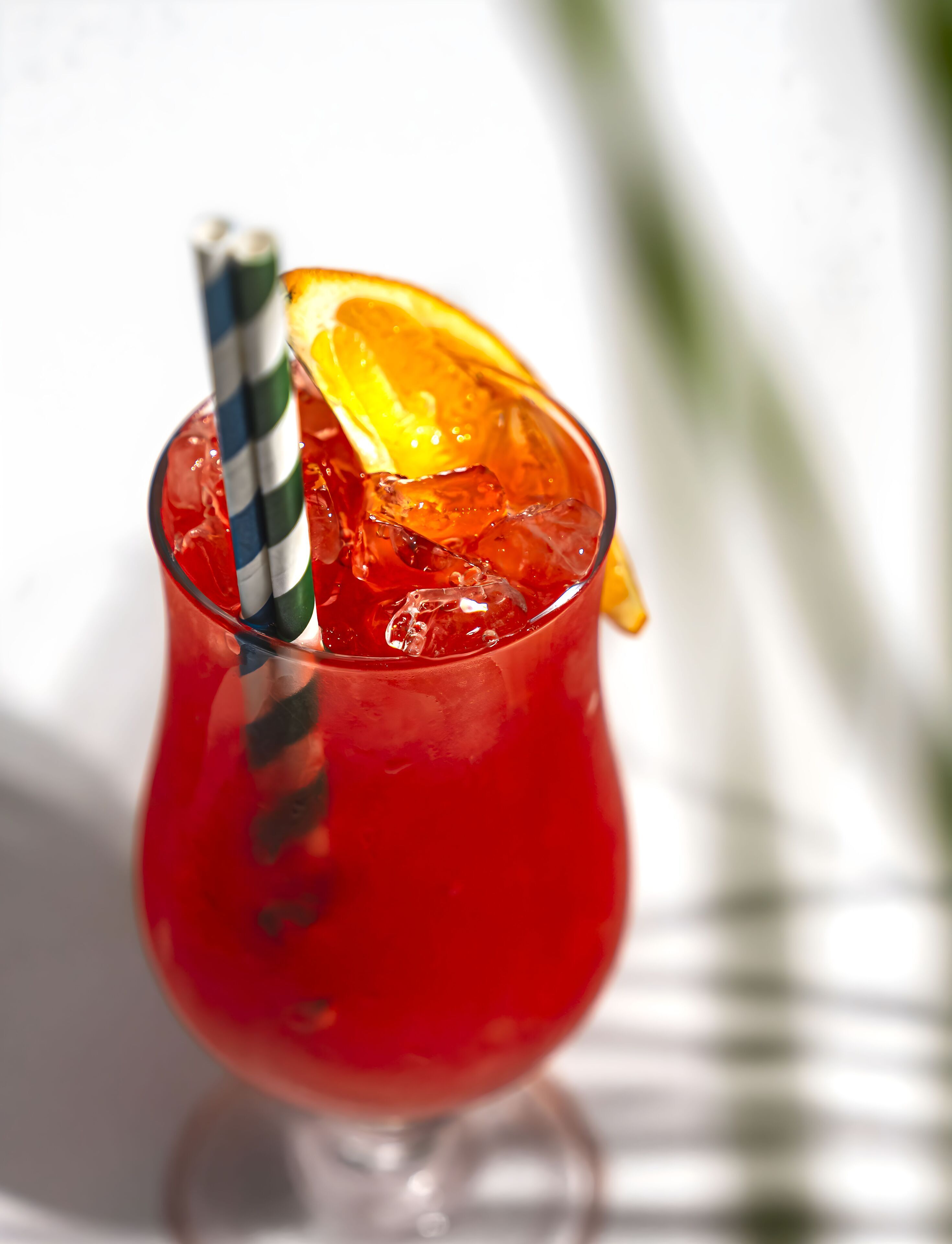 A cocktail glass with a striped straw, ice cubes, and an orange slice.