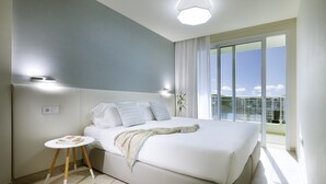 Een moderne slaapkamer met een groot bed, een klein nachtkastje en uitzicht op het balkon.