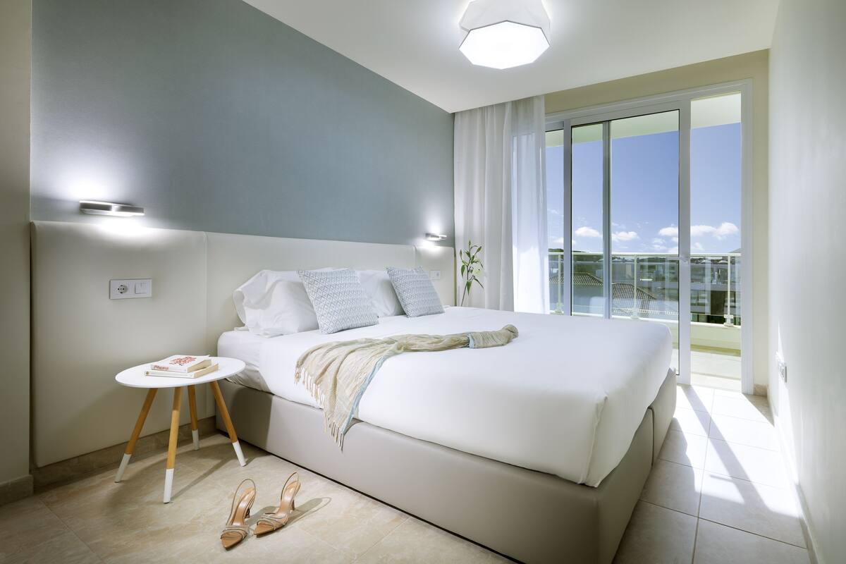 Een moderne slaapkamer met een groot bed, een klein nachtkastje en uitzicht op het balkon.