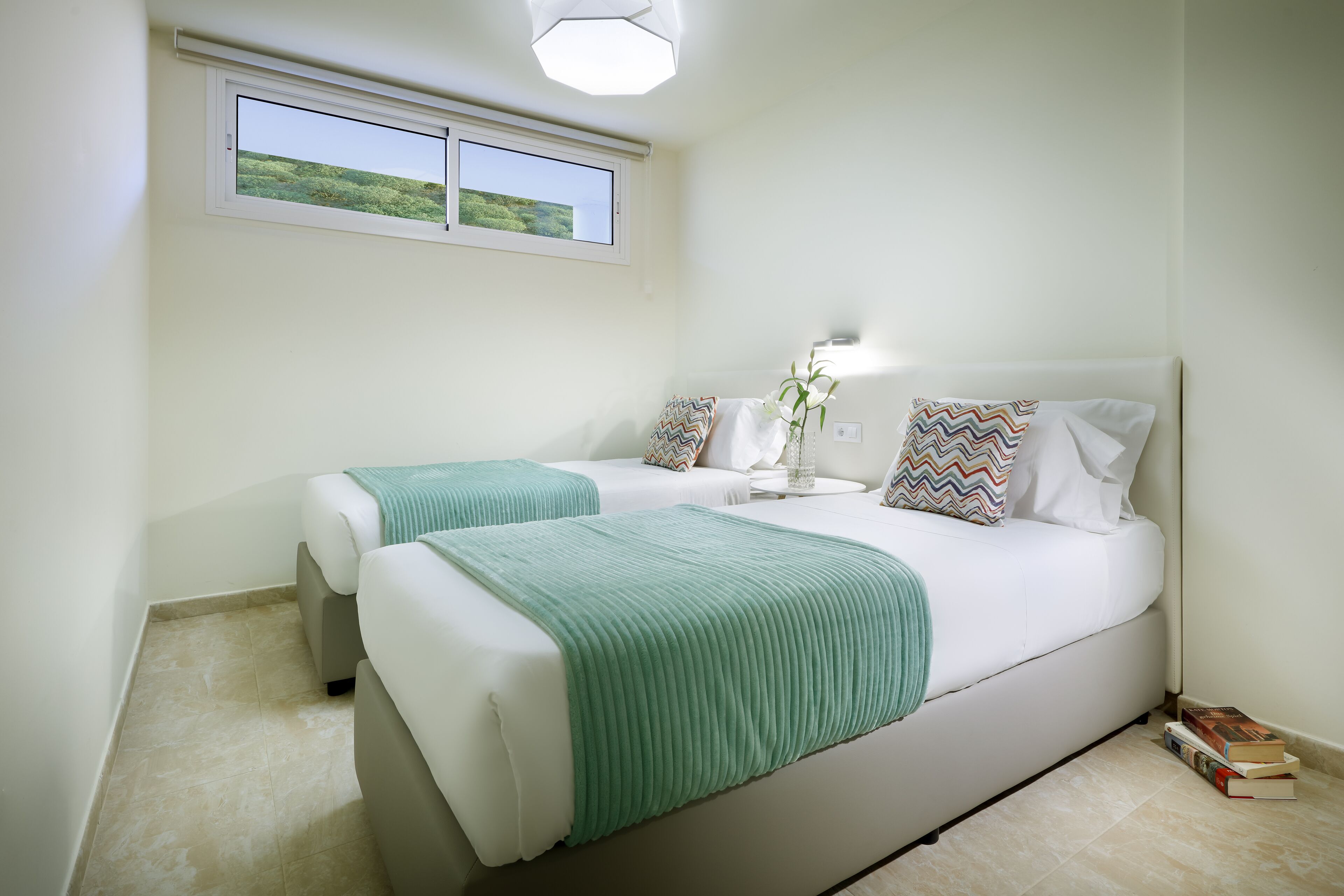 A bedroom with two beds, a window, and a nightstand with a lamp.